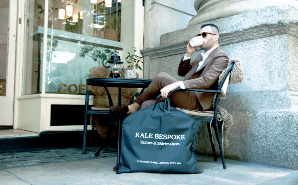 Man in bespoke brown suit sits and drinks coffee outside cafe